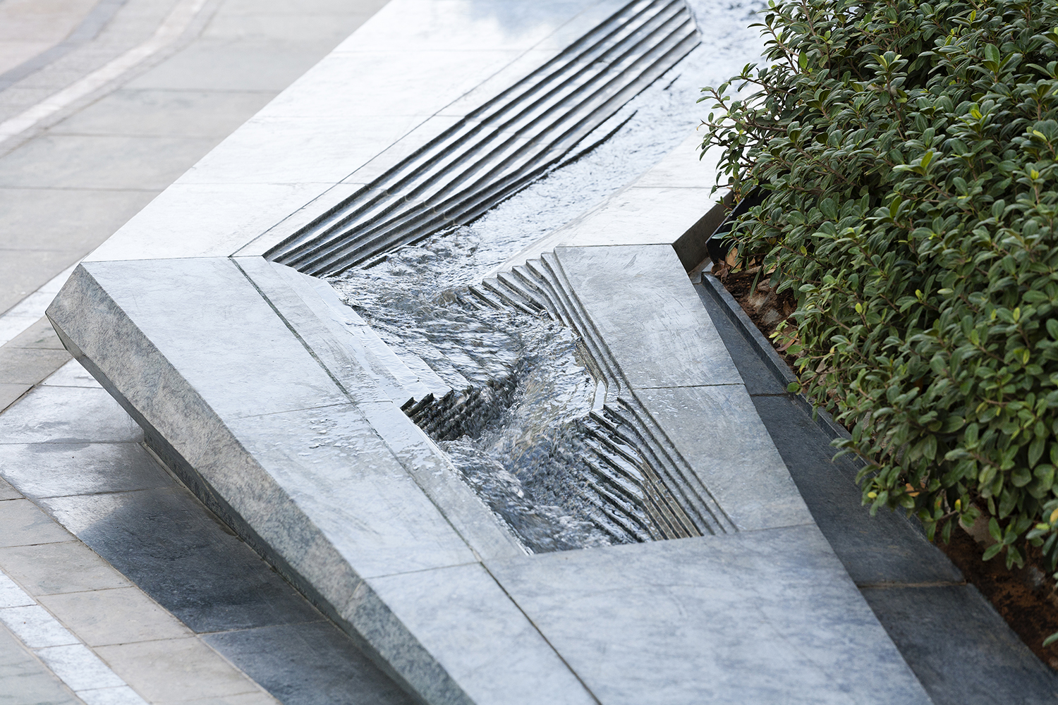 Water features are incorporated into long stone benches and the surface texture is finished with ornate grooves creating a rippling effect  