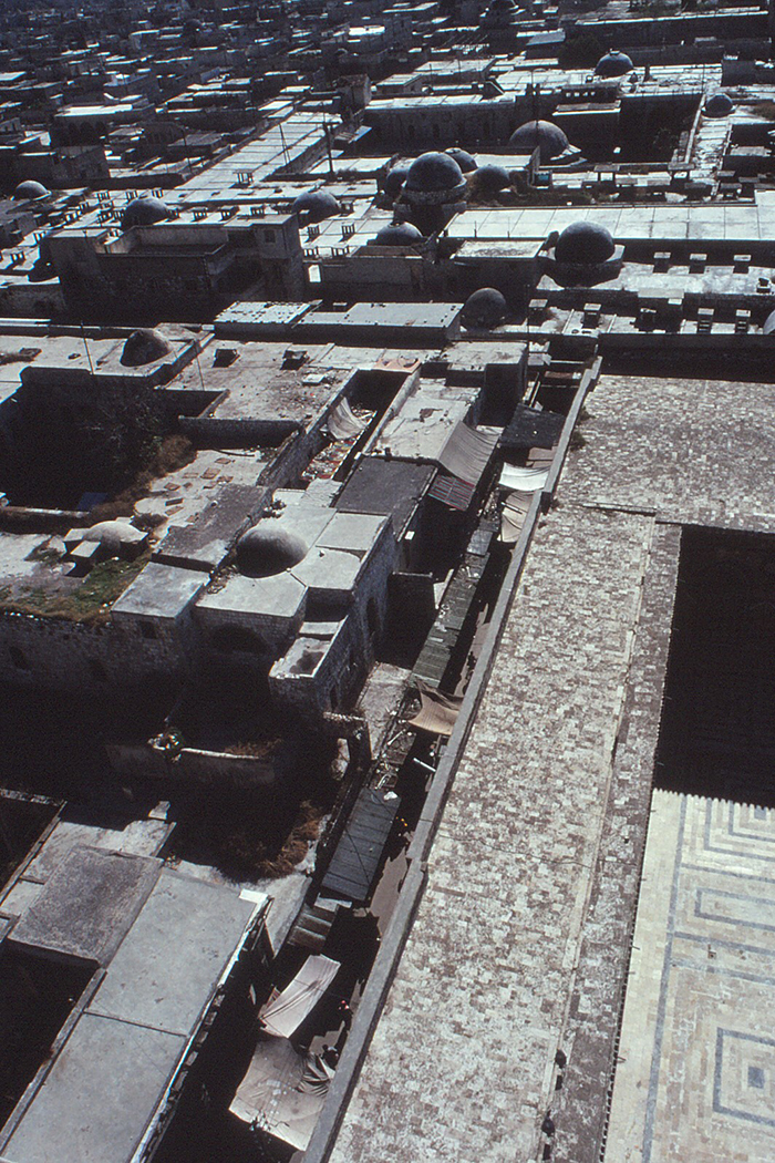 Aerial view accross the city rooftops, the Madrasa al-Halawiyya, the souqs. The corner of the mosque's courtyard is visible.