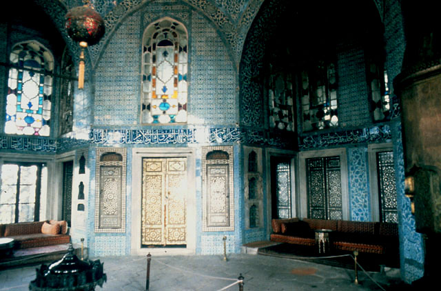 Interior view of the Baghdad Kiosk, showing decoration with divans in recesses, mother-of-pearl inlay on shutters and cuerda seca tiles on the walls.  The tile freeze below the window level bears the Verse of the Throne (Ayet-el-Kürsi) from the Koran