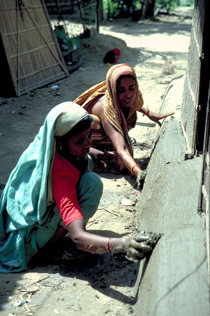 Women apply mud to the foundation of a house