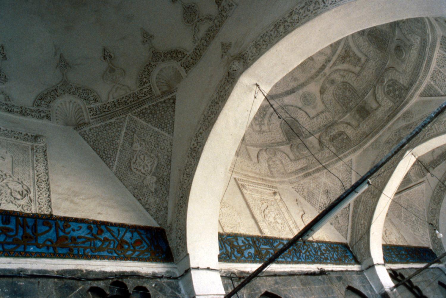 Interior dome ornately decorated with geometric patterns and Quranic inscriptions in carved gypsum