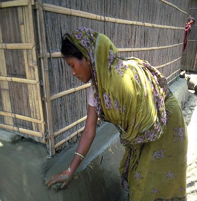 Woman applies mud to the foundation of a house