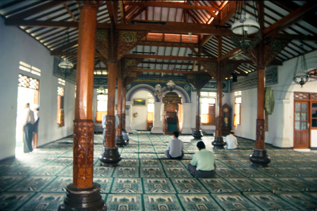 Interior view towards qibla wall showing carved wooden columns and inlaid gold