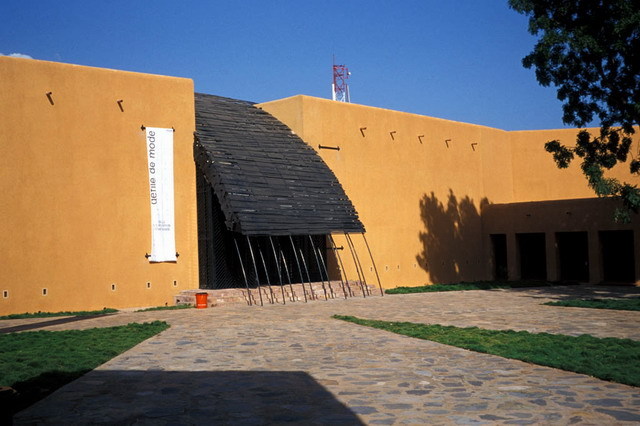 Exterior view; clay-finished wall with entrance shaded by curved screen
