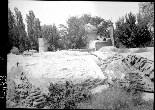 General view of a ruined mausoleum. The dome is still standing, as well as parts of the wall and two hexagonal engaged corner towers. A number of tombstones are in front of the mausoleum