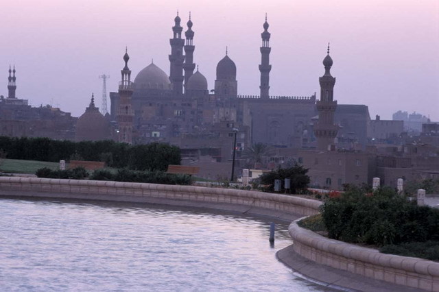 View of artificial lake at dusk, looking south. The domes and minarets of Sultan Hasan and Al-Rifa'i Mosques are silhouetted in the background, while the Khayrbak Complex and Amir Aqsunqur Mosque are seen at center in the Darb al-Ahmar neighborhood