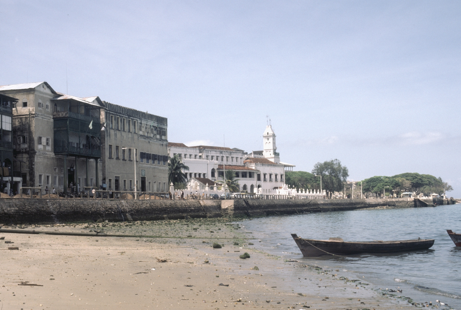Waterfront view, looking west, Sultan's Palace partially visible in distance, with House of Wonders clock tower. The pipe on the beach is a sewage pipe leading to the sea.