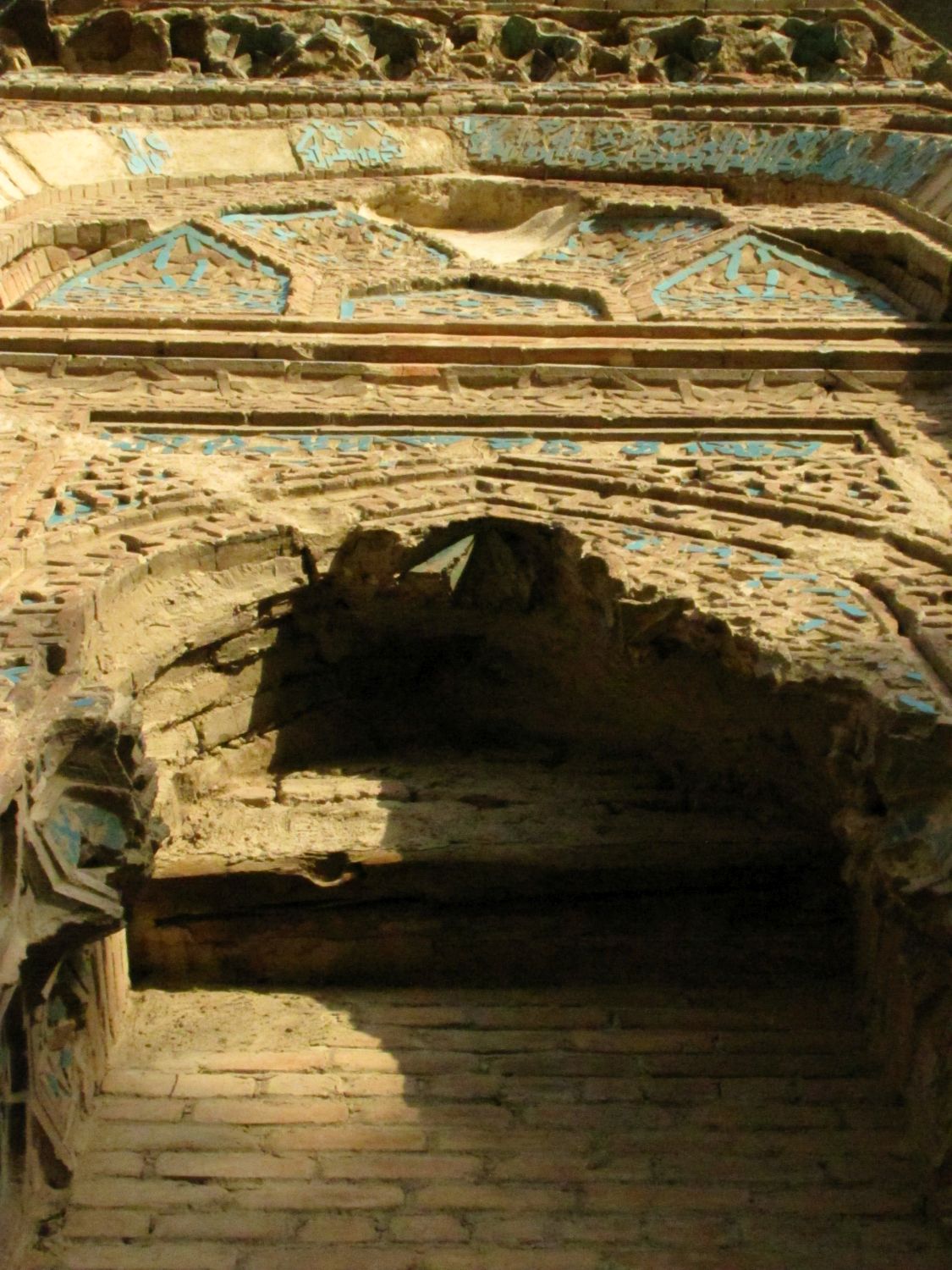 Detail view up at top of portal, with damaged muqarnas, partially glazed tiles and brickwork
