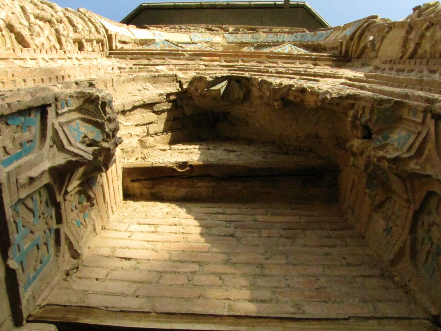View up at top of portal, from under its outer edge, at damaged muqarnas, partially glazed tiles and brickwork