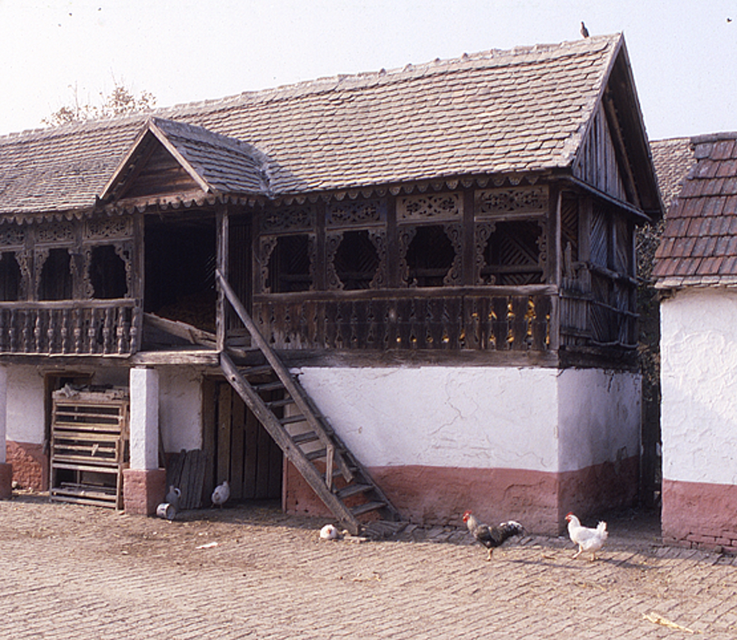 <p>Behind the gates and the village street outside, the wooden ambar (granary) and koš (corncrib) sit over a masonry base where poultry, tools and equipment are kept. The lower level is constructed of soft bricks covered with a plaster coating and painted to accent the base. The roof is wood-framed and covered with clay tiles.</p>