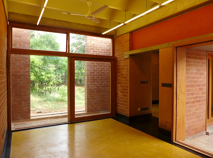 Interior view of the south office building showing the exposed masonry walls, full height teakwood windows, curved roof channels and ochre flooring