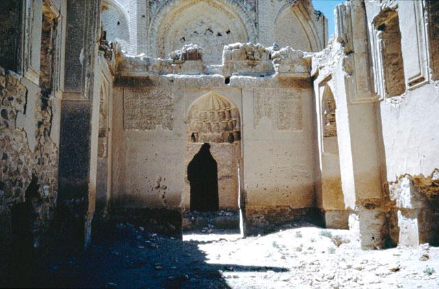 Interior view from the main iwan of khanqah, showing doorway with muqarnas hood flanked by inscriptive panels. The upper portion of tomb tower is visible above doorway wall