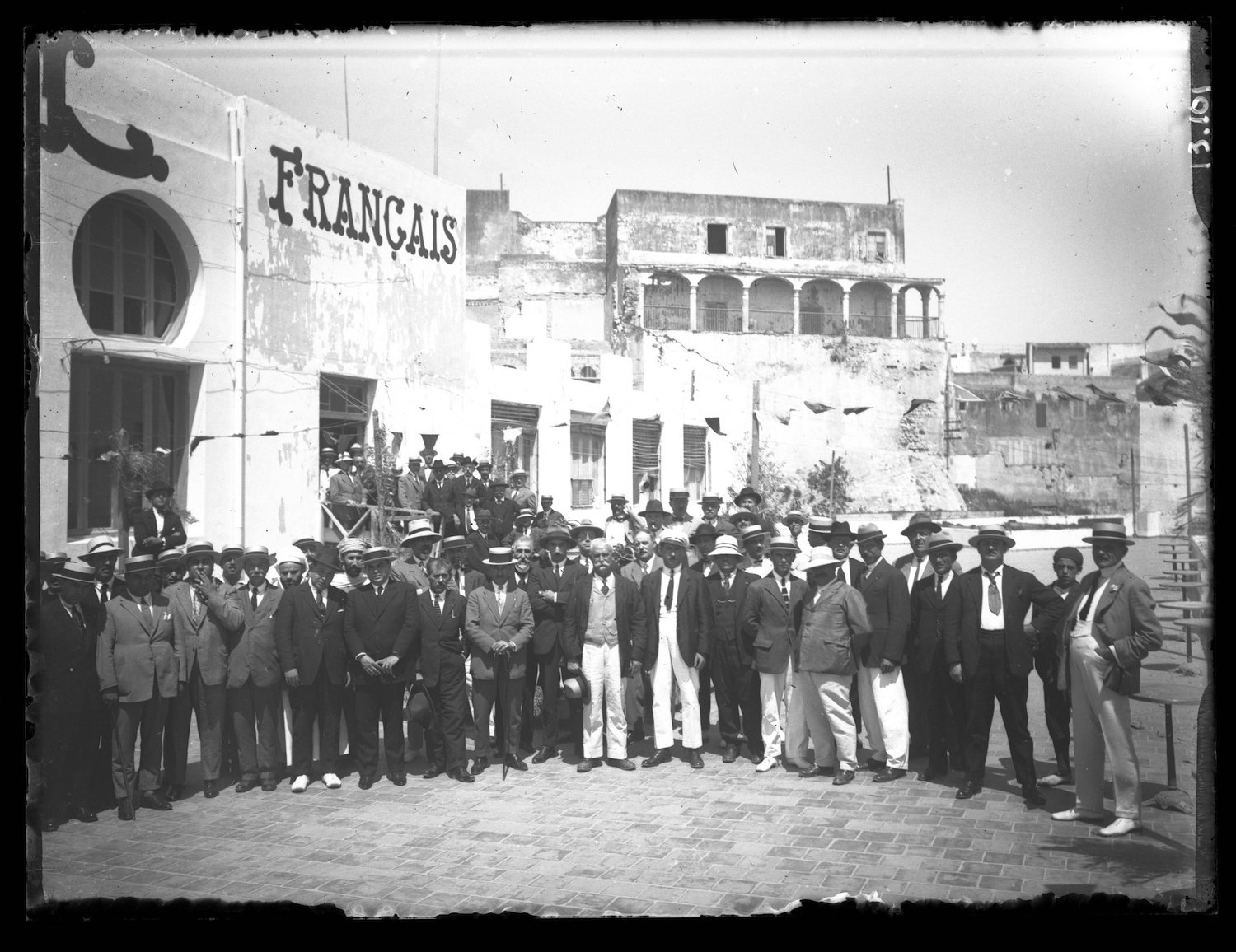 A large group of men in suits and hats pose outside of a the Kursaal 