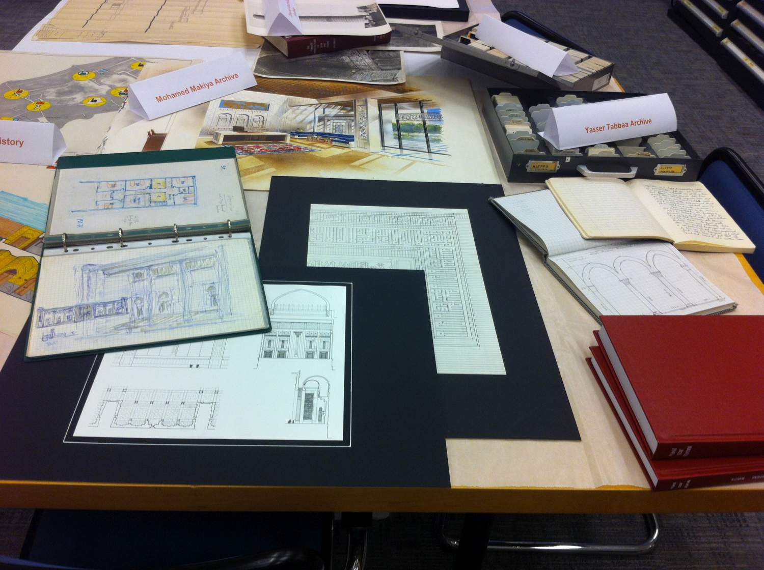 Mohamed Makiya Archive drawings, sketches, and interior design watercolor study (center 3 items), and Yasser Tabbaa Archive notebooks and slides at middle right (above red special collection volumes)