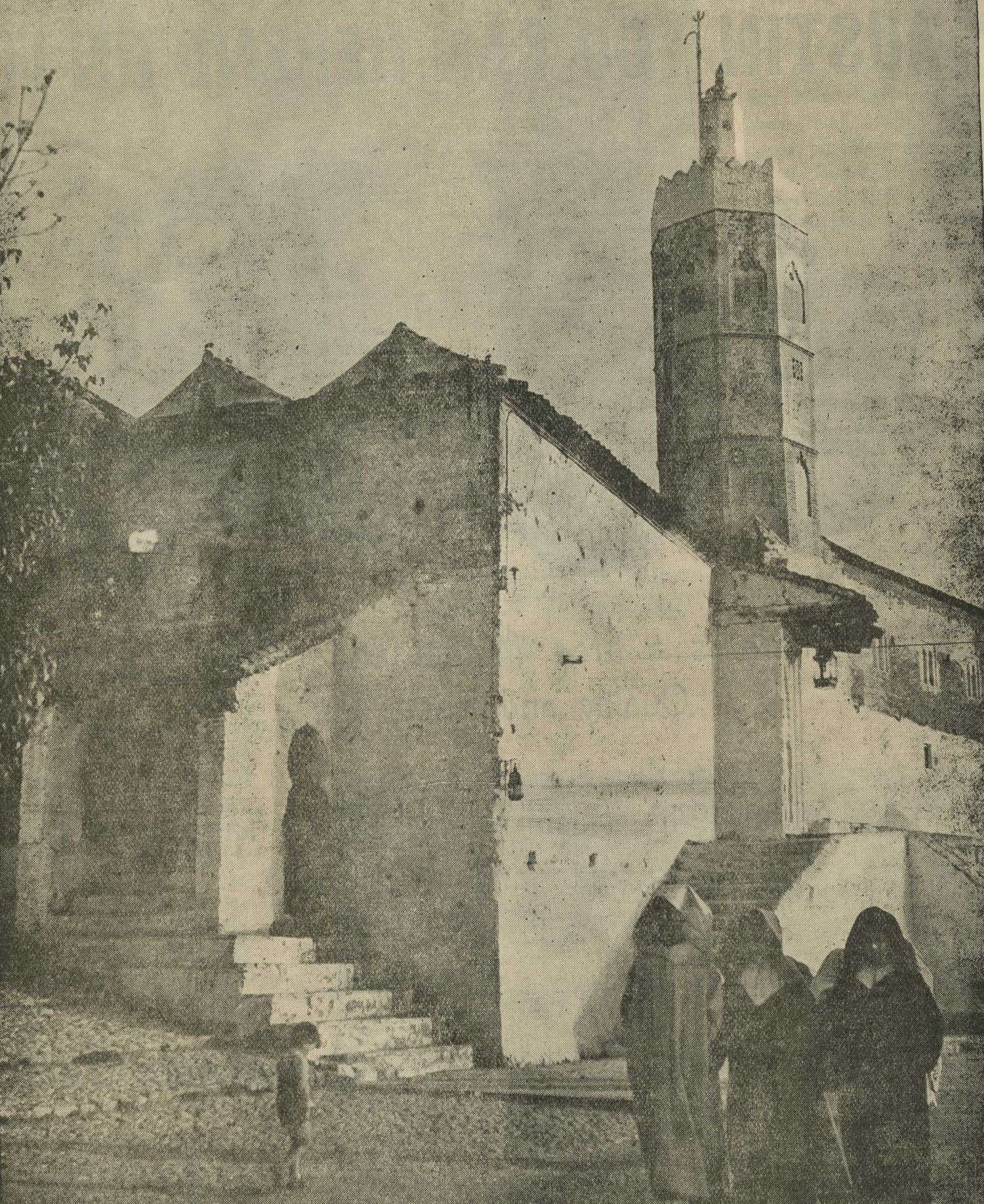 Jama' al-Kebir - Newspaper photo: Three men in djellabas and a child on the square outside the mosque with minaret, arched doorway at the steps. 
