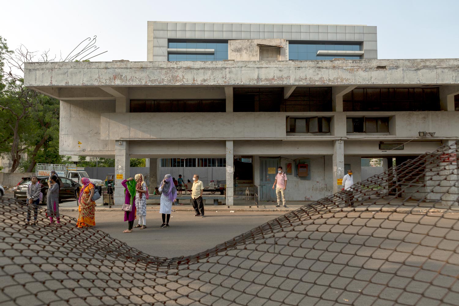 <p>Front elevation of the Navrangpura Bus Terminus. merging with Ahmedabad Municipal Corporation's new multi-level parking &amp; commercial complex in the background. Bent fence in the foreground.</p>