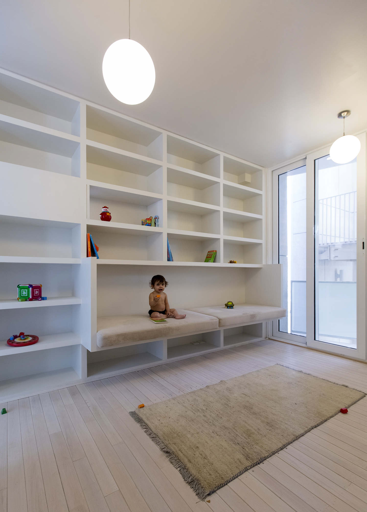 Interior view of the kids’ bedroom on the third floor illustrating the shelving system, the embedded kids’ bed, and how the staircase provides ample natural light via the light shaft
