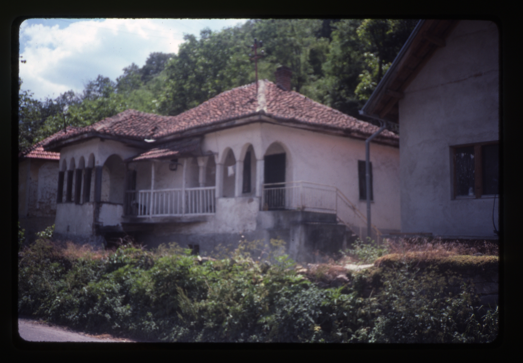 <p>This dwelling (kuća) has numerous renovations and modifications. The traditional arched entry porch, separate elevated porch (čardak) and roman style clay tile roof have survived the changes. The exterior renovations have created a more substantial stair and metal railing leading to the entry and a diagonal bridge connection from the entry porch to the čardak on the left.</p>