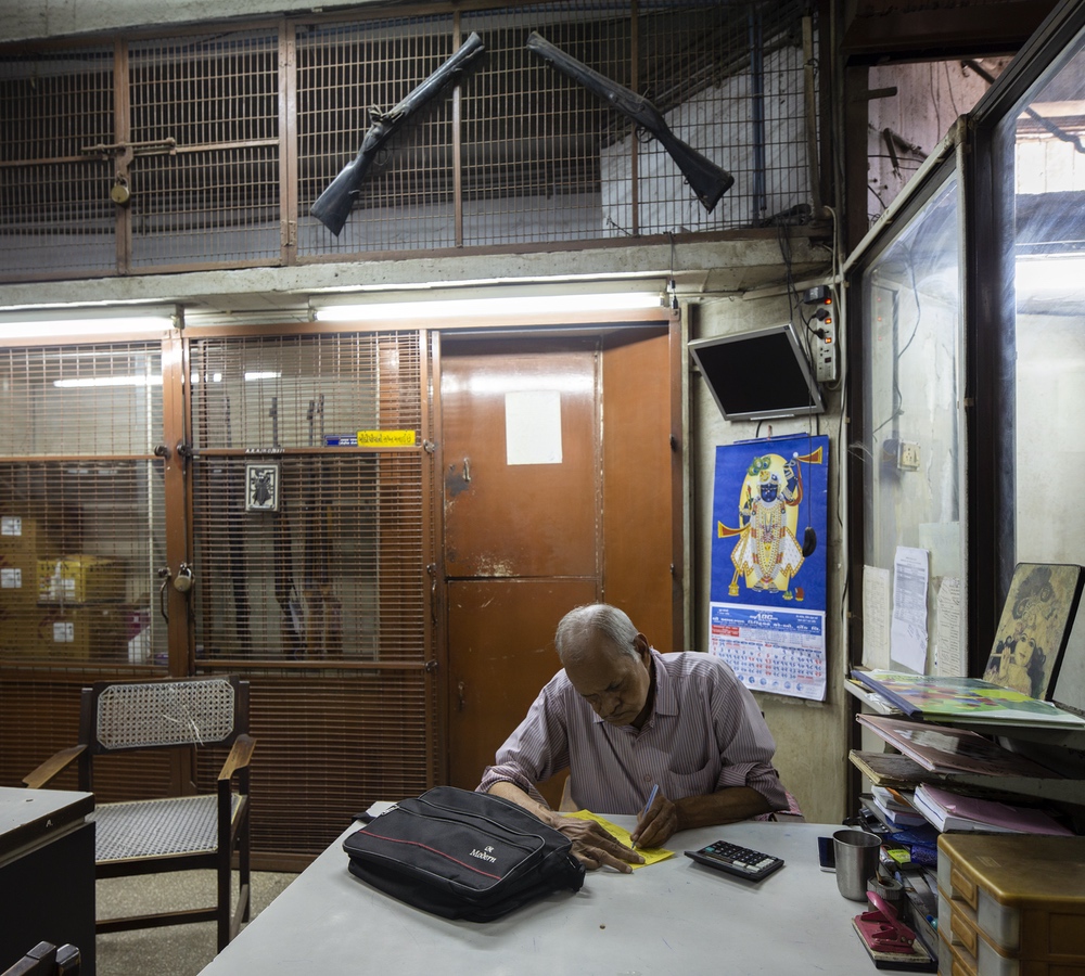 <p>Mr Chandrakant Shah at his table in the office of Ahmedabad Rifle Association. In the background are the airguns which the association now sells.</p>