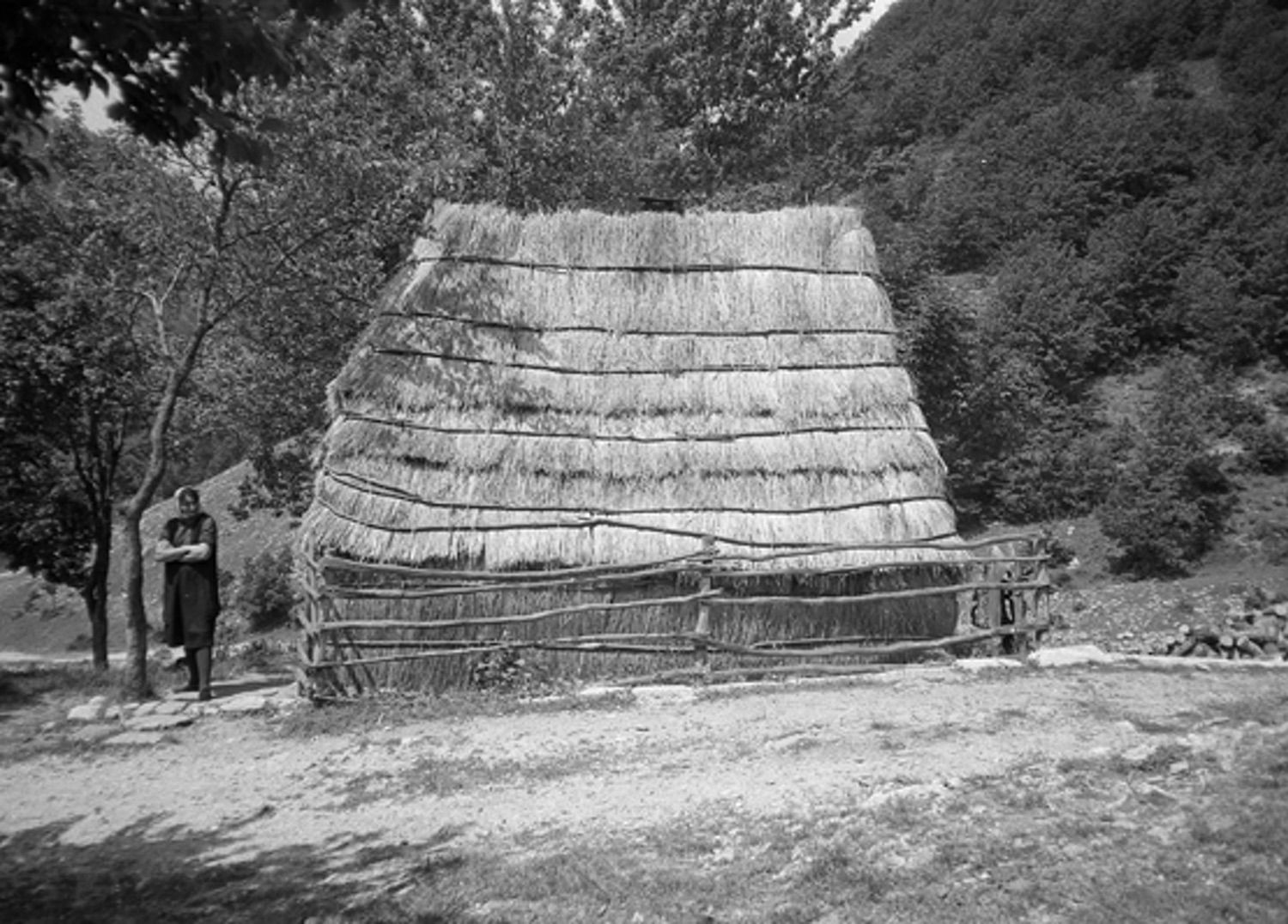 <p>Rijeka is a village on the road that parallels the Zalomska River in northeastern Herzegovina. In this remote highlands area, people like the woman pictured here continued to inhabit dwellings enclosed in straw, probably as seasonal pasture shelters. The fence around the house may protect the straw from hungry animals.</p>