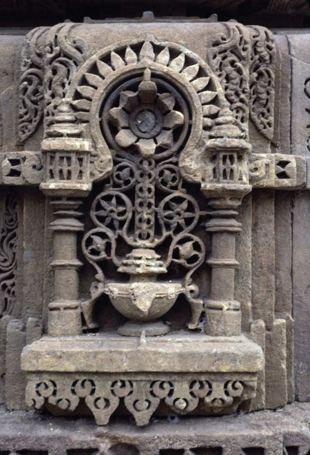 Detail view of carved motif on minaret showing vase, scrolling vine, and large flower within a niche.